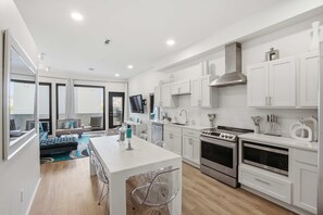 Une cuisine moderne avec des meubles blancs, un îlot central, des appareils électroménagers en acier inoxydable et un coin repas comprenant un canapé et des chaises.