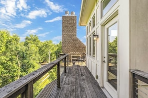 A wooden deck with a brick chimney, a glass door, and a view of trees.