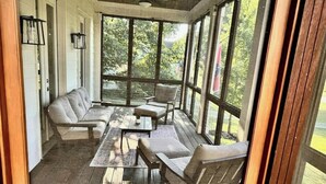 A covered porch with a sofa, chairs, and a table. - Recently-built all-suite with two porches, firepit, crow's nest, & widow's walk (Franklin)