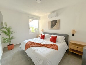 A bedroom with a bed, a potted plant, a bedside table, and a wall-mounted lamp. - Estancia Cómoda en Centro Vallarta - 4 (Puerto Vallarta)