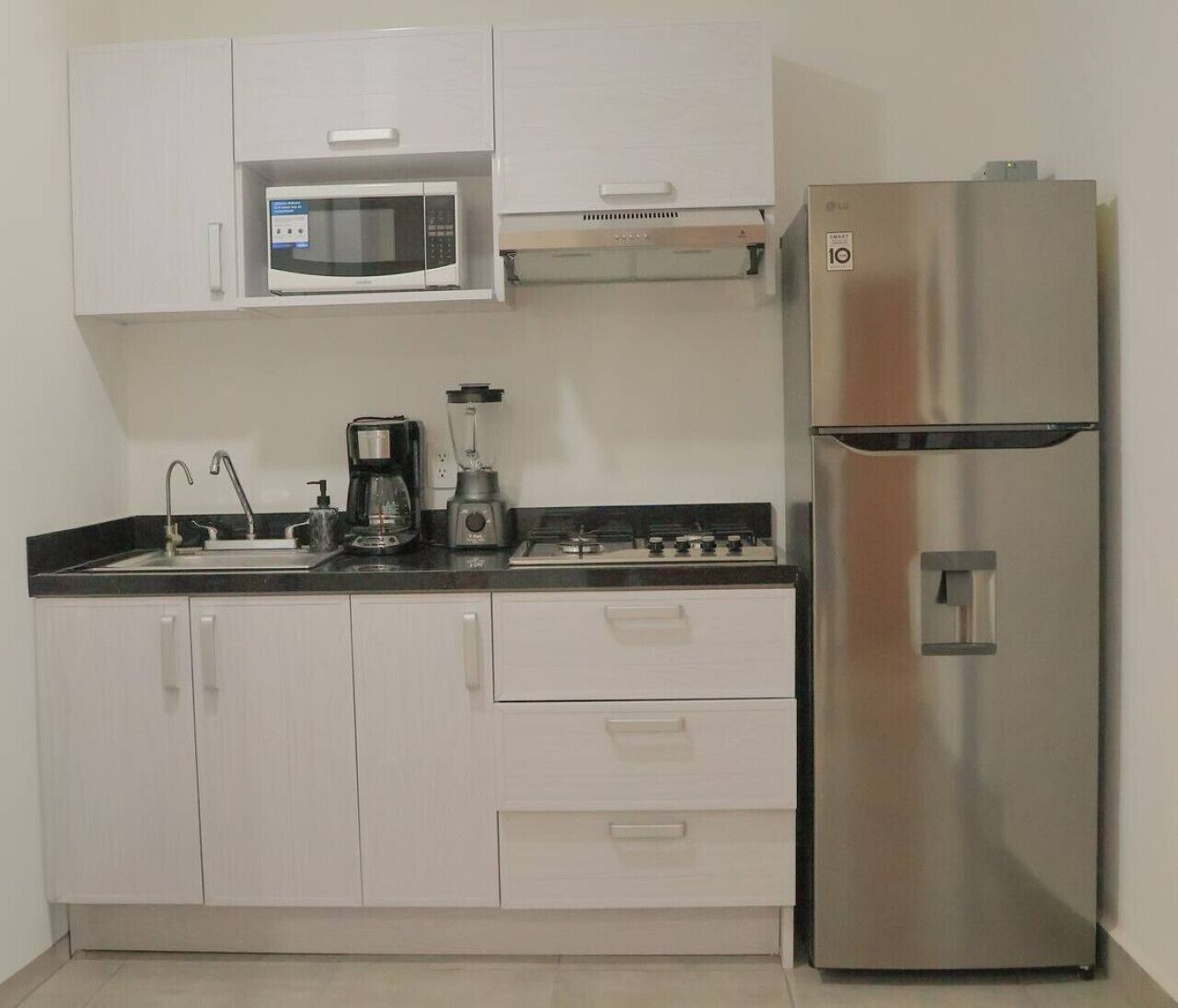 A kitchen with white cabinets, a stainless steel refrigerator, a microwave, a coffee maker, and a stove.