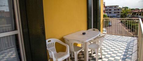 Un balcon avec un sol à carreaux, une table, des chaises et un mur jaune.