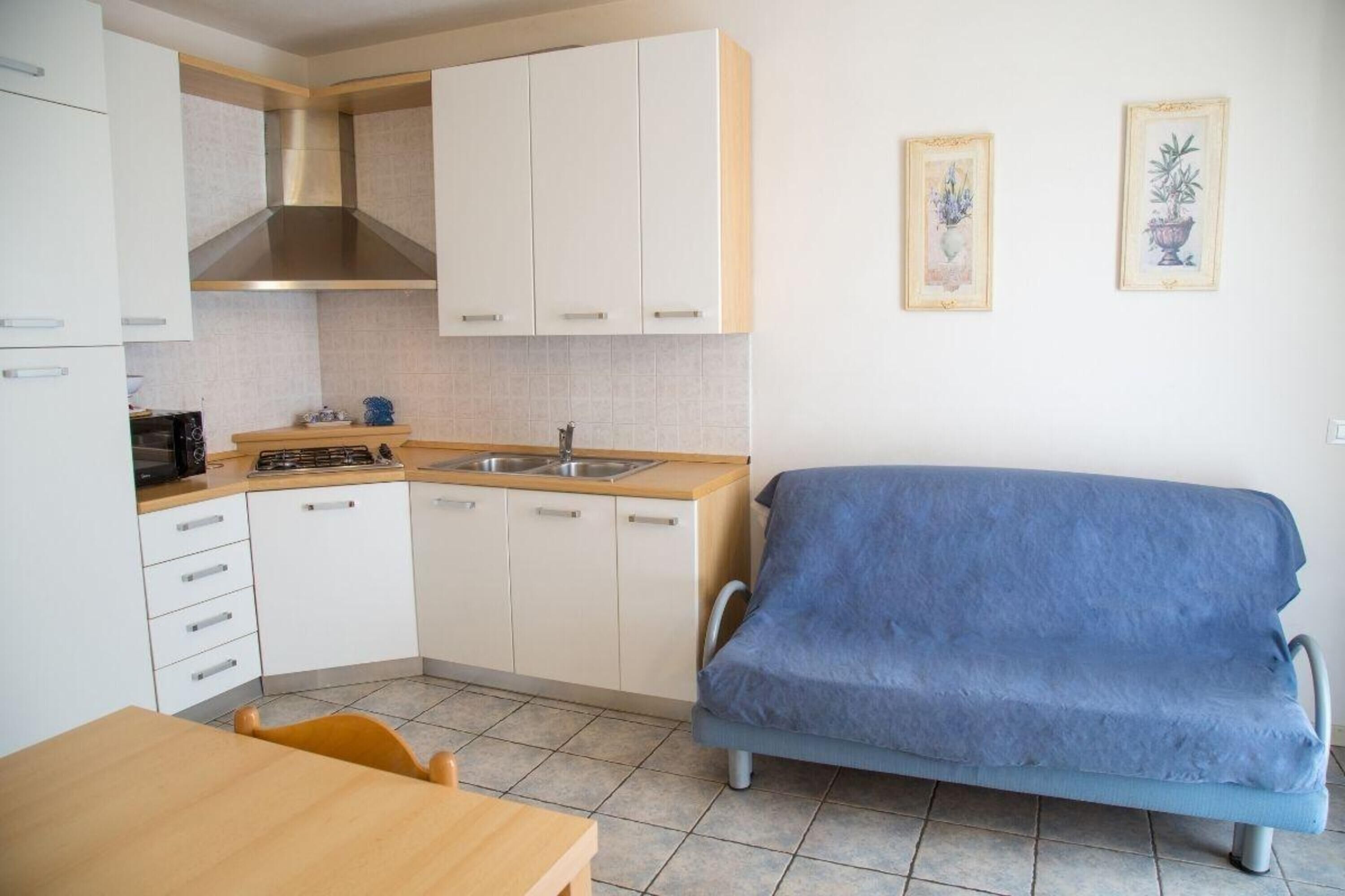 Une cuisine de taille réduite avec des meubles blancs, une cuisinière et un évier. On y trouve un canapé bleu et une table en bois avec des chaises.