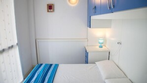Une petite chambre avec un lit simple, une table de chevet, une lampe et une armoire bleue.