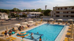 Une piscine entourée de bâtiments, avec des chaises longues et des parasols.
