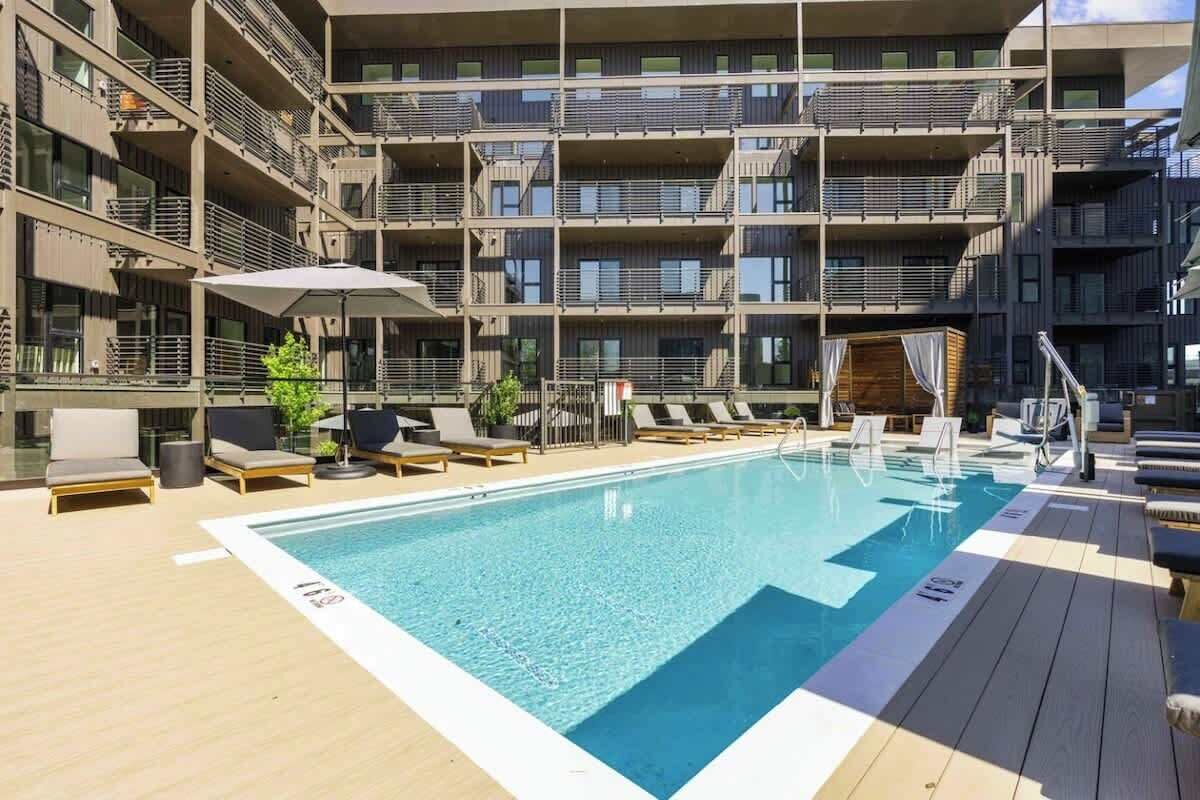 A multi-story building with a swimming pool, sun loungers, and a covered seating area.