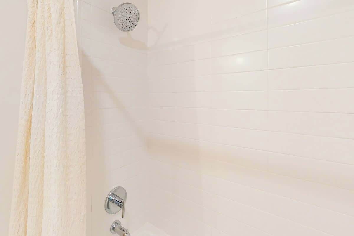 A shower area with white tiles, a showerhead, and a curtain.
