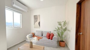 Un salon avec un canapé gris, une table basse en bois, une plante en pot et une grande fenêtre.