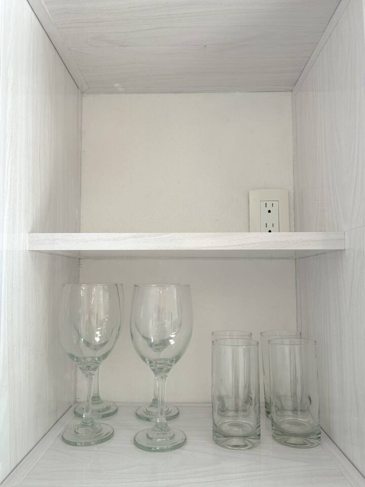 Een witte plank met drie wijnglazen en vier glazen.