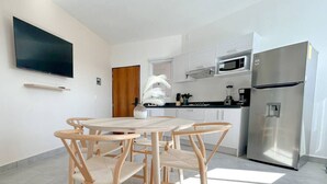 Une cuisine moderne avec des armoires blanches, un réfrigérateur en acier inoxydable et un téléviseur à écran plat fixé au mur.