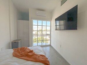 A bedroom with a bed, a wardrobe, a small table, and a large window with a view of buildings. - Estancia Cómoda en Centro Vallarta - 3 (Puerto Vallarta)