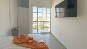 A bedroom with a bed, a wardrobe, a small table, and a large window with a view of buildings. - Estancia Cómoda en Centro Vallarta - 5 (Puerto Vallarta)