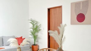 A modern living room with a round wooden table, two chairs, a sofa, a potted plant, and a door. - Estancia Cómoda en Centro Vallarta - 5 (Puerto Vallarta)