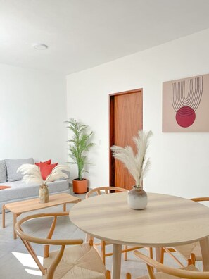 A modern living room with a round wooden table, two chairs, a sofa, a potted plant, and a door. - Estancia Cómoda en Centro Vallarta - 5 (Puerto Vallarta)