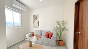 A living room with a grey sofa, a wooden coffee table, a potted plant, and a large window. - Estancia Cómoda en Centro Vallarta - 5 (Puerto Vallarta)