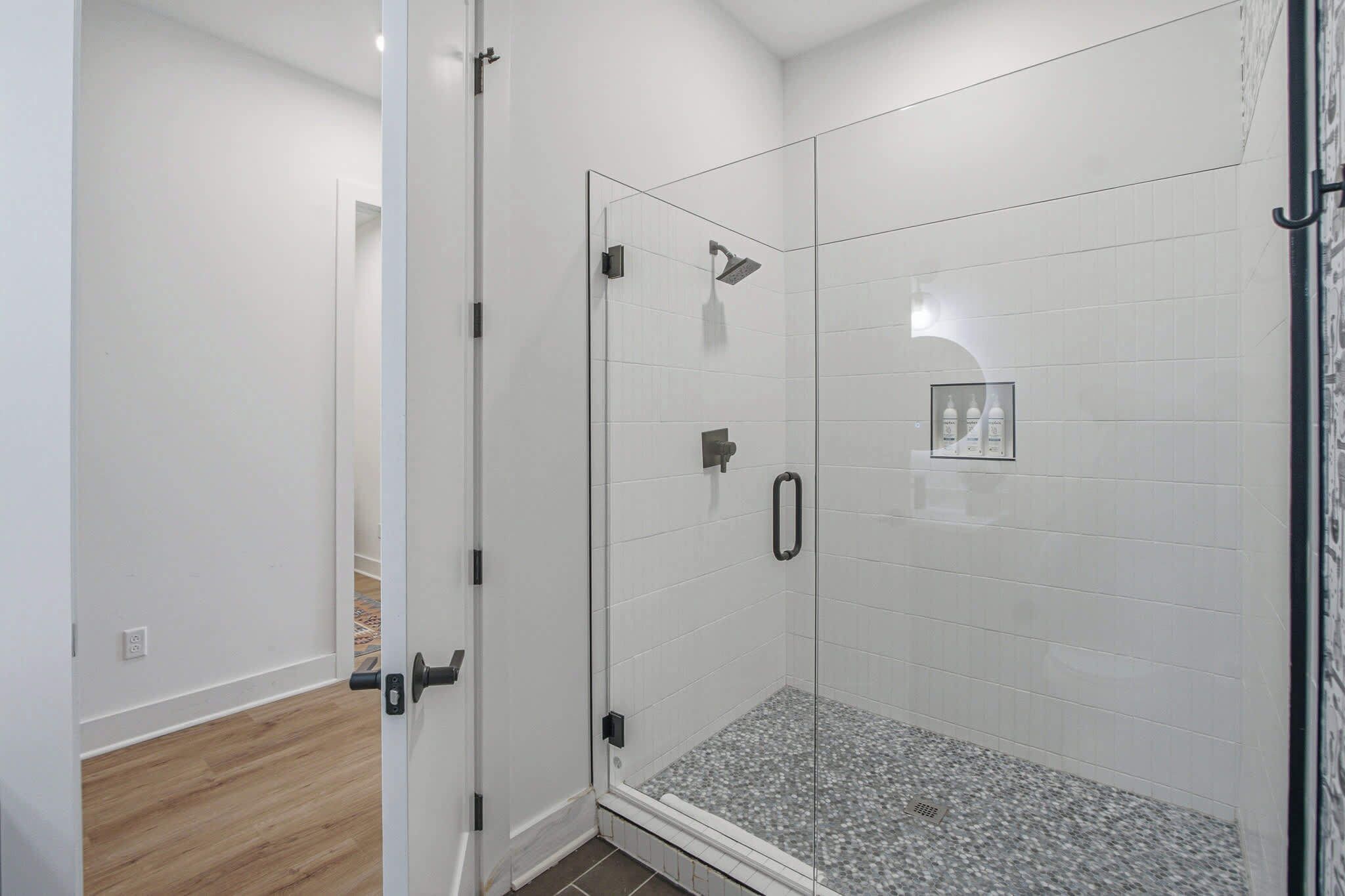 Een douche met glazen wanden, een betegelde vloer, een deur met een hendel en een klein lijstwerk met een afbeelding aan de muur.