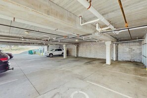 A parking garage with concrete floors and walls, visible pipes and ducts on the ceiling, and a white car parked in one of the spaces. - Dog-friendly condo with central AC & rooftop deck access - walk everywhere (Nashville)