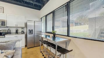 A modern kitchen with stainless steel appliances, a bar area with stools, and a large window with blinds.