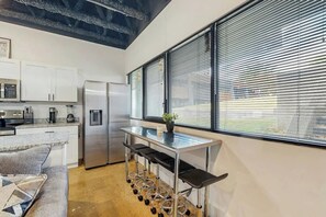 A modern kitchen with stainless steel appliances, a bar area with stools, and a large window with blinds. - Charming Condo Dog Friendly Stay Near Downtown (Nashville)