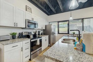 A modern kitchen with white cabinets, stainless steel appliances, granite countertops, and a large window with a view. - Charming Condo Dog Friendly Stay Near Downtown (Nashville)