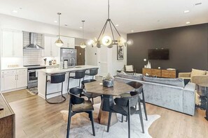 A modern kitchen with a central island, dining area with chairs, a sofa, and a TV mounted on the wall. - Spacious Modern Condo, Near Vanderbilt & Broadway (Nashville)