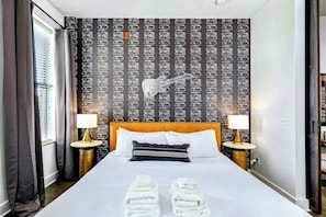 A hotel room with a bed, two bedside tables with lamps, a headboard, a patterned wallpaper, and a window with curtains. - West End Nashville Retreat, Near Vanderbilt & Park (Nashville)
