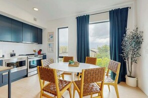 Eine moderne Küche mit integrierten Geräten, ein Essbereich mit rundem Tisch und Stühlen sowie ein großes Fenster mit Vorhängen.