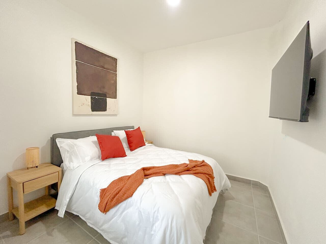 Une chambre à coucher avec un lit, une table de chevet, un téléviseur fixé au mur et un tableau.