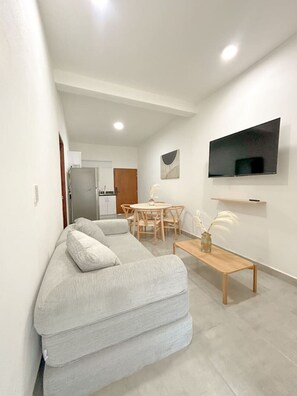 Ein modernes Wohnzimmer mit einer Couch, einem Esstisch und einem an der Wand befestigten Fernseher.
