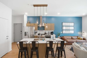 A modern kitchen with a central island, bar stools, a dining table, a sofa, and a coffee table in a living area. - Pool View Balcony, Near Attractions, Grill, Gym (Nashville)