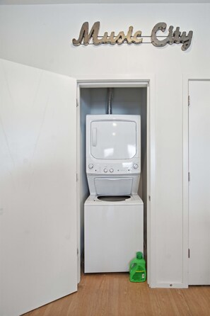A laundry room with a washing machine and dryer, a green detergent bottle on the floor, and a sign above that reads 'Music City'. - Pool View Balcony, Near Attractions, Grill, Gym (Nashville)