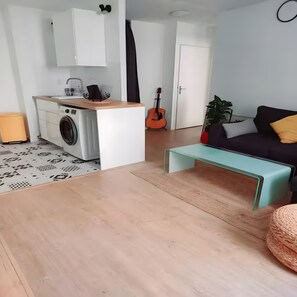 Ein gemütlicher Wohnraum mit Küchenzeile, einer Couch, einer Gitarre und einer Pflanze.