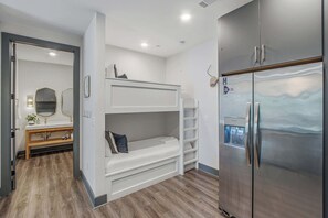 Ein kleines Hotelzimmer mit einem Etagenbett, einem modernen Kühlschrank und einem Holzwaschtisch mit Spiegel.