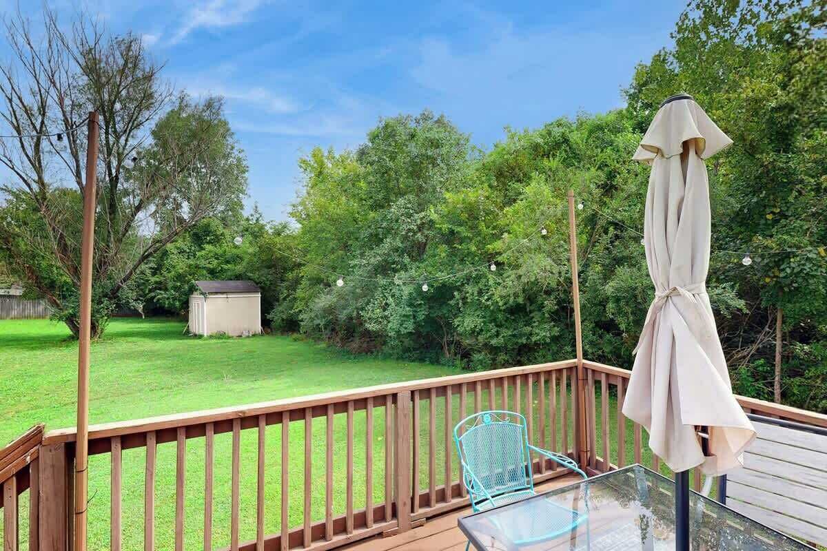 A deck with a glass table and chairs, a covered umbrella, and a wooden railing.