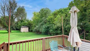 A deck with a glass table and chairs, a covered umbrella, and a wooden railing.