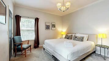 A hotel room with a bed, a chair, a lamp, and a window with curtains.