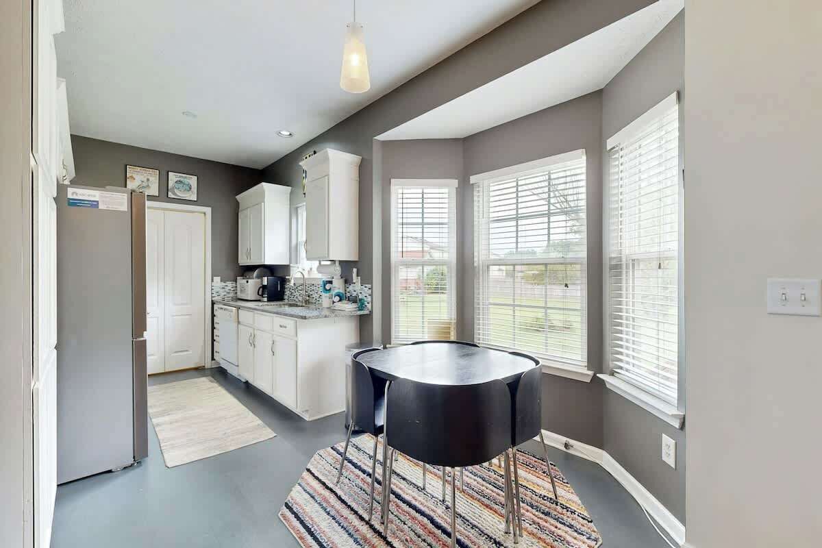 A modern kitchen with white cabinets, a black dining table, and a patterned rug.
