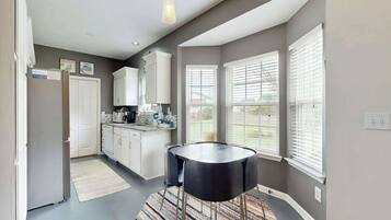 A modern kitchen with white cabinets, a black dining table, and a patterned rug.