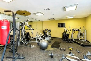Ein Fitnessraum mit Trainingsgeräten, einem roten Boxsack, einer Spiegelwand und einem Laufband.