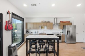 A modern kitchen with a central island, bar stools, a refrigerator, and a guitar on the wall. - Skyline-View Condo with Seasonal Pool Gym Access (Nashville)