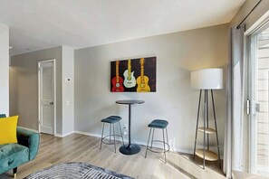 A modern living room with a sofa, a round table, two bar stools, a painting, and a floor lamp. - Third-Floor Riverfront Condo w Balcony, Pool, & Fast WiFi - Near Broadway (Nashville)