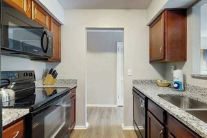 A kitchen with wooden cabinets, a stainless steel microwave, a stove, and a granite countertop. - Third-Floor Riverfront Condo w Balcony, Pool, & Fast WiFi - Near Broadway (Nashville)