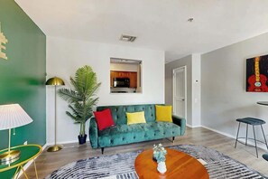 A living room with a green sofa, a coffee table, a lamp, and a plant. - Third-Floor Riverfront Condo w Balcony, Pool, & Fast WiFi - Near Broadway (Nashville)