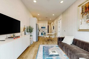 A living room with a flat-screen TV, a sofa, a coffee table with books, a plant, and a kitchen in the background. - Stylish condo with balcony, high speed internet, WD and elevator (Nashville)