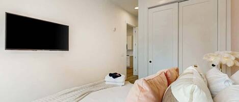 Une chambre à coucher comprenant un lit, un téléviseur à écran plat, une armoire et une porte donnant sur une salle de bain.