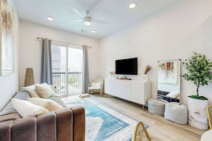 A modern living room with a sofa, a flat-screen TV, a large window, and a ceiling fan. - Stylish condo with balcony, high speed internet, WD and elevator (Nashville)