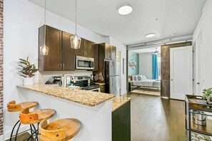 A modern kitchen with granite countertops, stainless steel appliances, and wooden bar stools. - Modern Midtown loft with all-new interior & amazing park views - near Vanderbilt (Nashville)