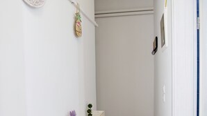 En smal hall med en vit vägg, en hylla med små växter, en brandsläckare och en dörr på höger sida.