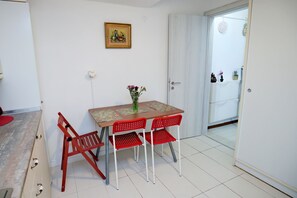 Spiseområde med bord, stole, en vase med blomster, et maleri på væggen og en dør der fører til en balkon.
