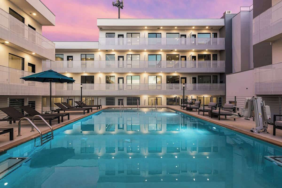 Ein modernes Hotel mit zentralem Pool, mehreren Balkonen und einem Abendhimmel.